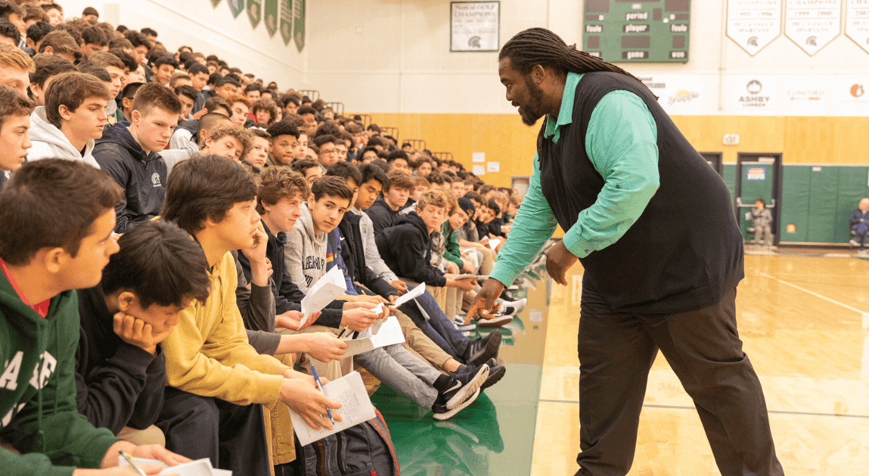 A teacher and a large group of kids at a school assembly.
